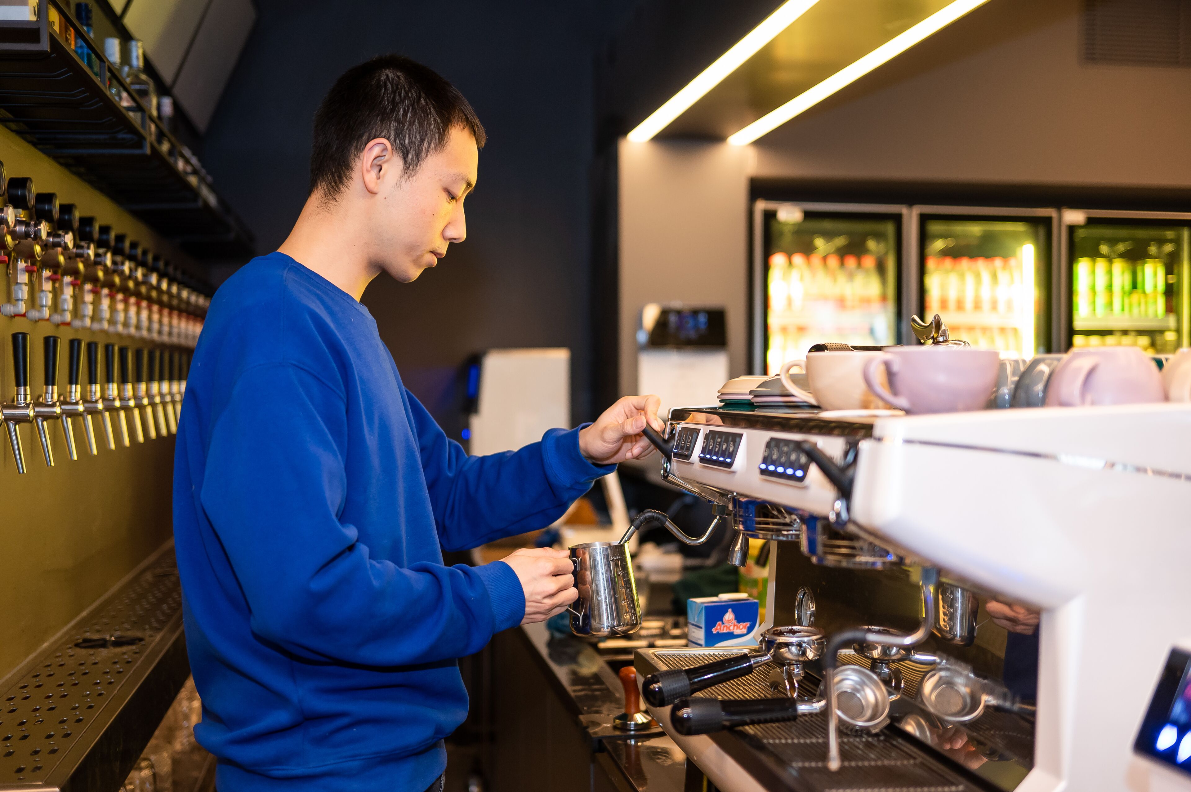 A barista in a blue sweater preparing a drink at an espresso machine.