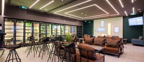 Un café moderne doté d’espaces pour s’asseoir, d’un réfrigérateur rempli de boissons et d’un écran de projection diffusant des informations.