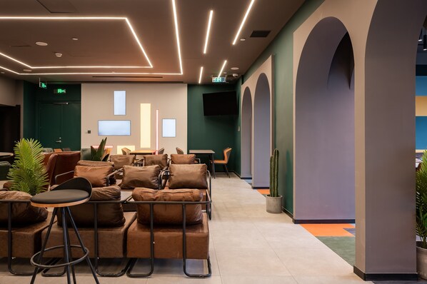 A modern lounge area with leather sofas, a bar stool, and a flat-screen TV mounted on the wall.