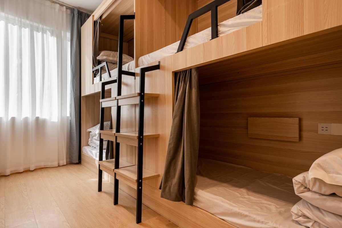 Une chambre avec des lits superposés en bois, une étagère et une prise de courant.