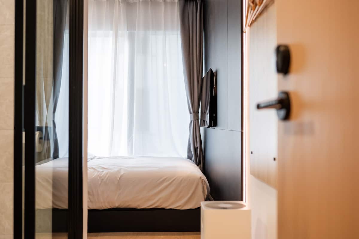 Une chambre d’hôtel moderne, équipée d’un lit, d’une table de chevet, d’un téléphone fixé au mur et d’une porte avec une poignée.