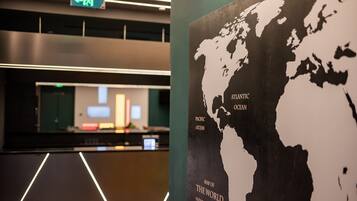 Un mostrador de recepción con un monitor de computadora, un letrero de salida verde y un cartel con un mapa del mundo.
