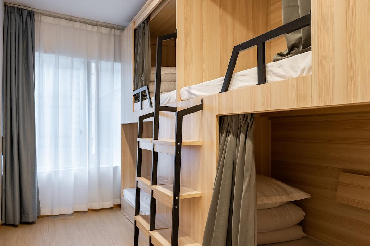 Une chambre avec des lits superposés, des murs en bois et une fenêtre ornée de rideaux légers.