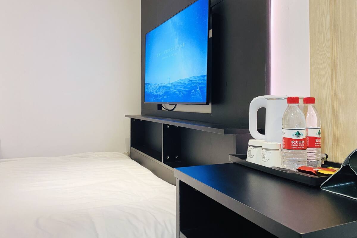 Une chambre d’hôtel avec un lit, un téléviseur posé sur un meuble et une table avec des bouteilles d’eau et une bouilloire.