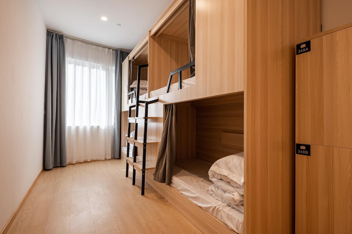 Une chambre avec des lits superposés, une armoire en bois et une fenêtre avec des rideaux.