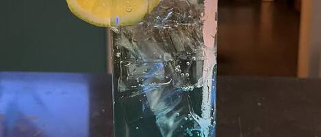 A glass with a blue liquid, ice cubes, and a lemon slice with a pink straw.