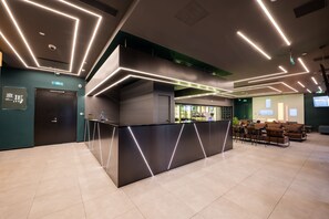 A modern reception area with a black counter, green walls, and a seating area with brown sofas.