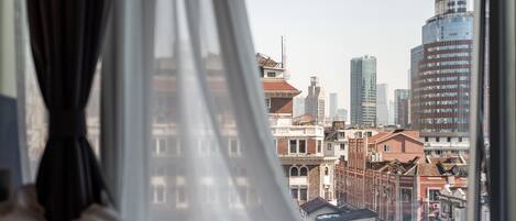 Blick aus einem Fenster mit transparenten Vorhängen auf eine Stadtlandschaft mit modernen und historischen Gebäuden.