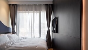 Ett modernt hotellrum med en stor säng, en platt-TV som är monterad på väggen och utsikt över staden genom tunna, genomskinliga gardiner.