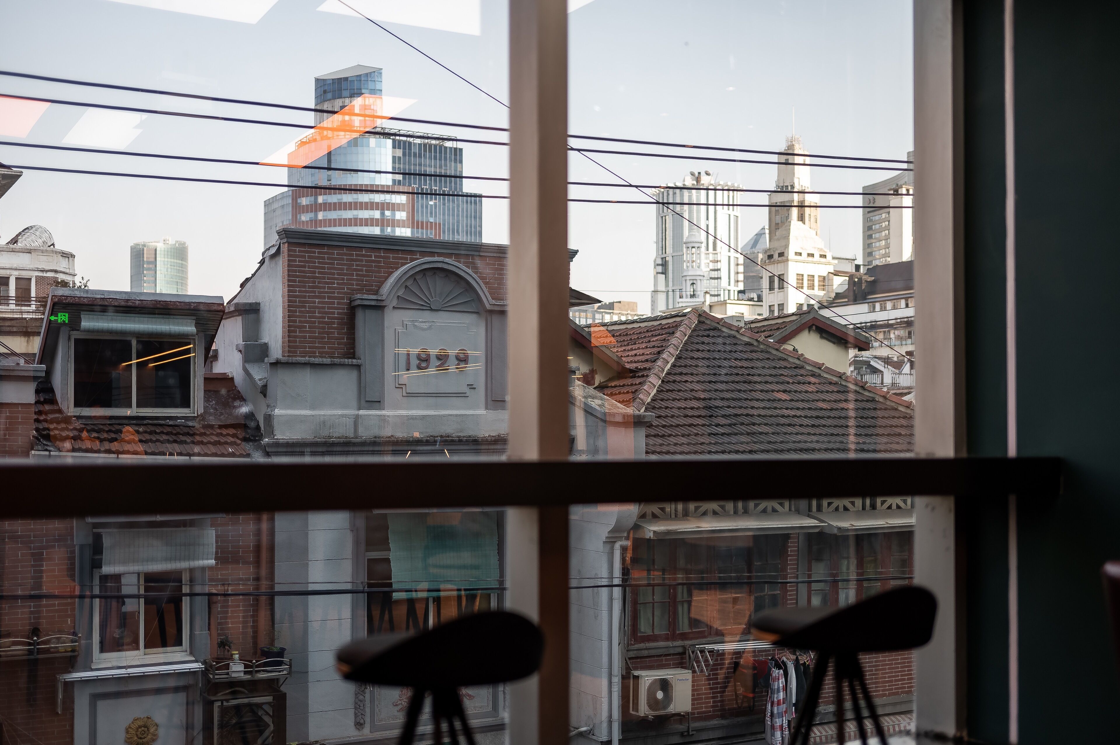 A view through a window of a building with multiple floors, featuring a mix of modern and traditional architecture, including a prominent clock tower and various buildings with different roof styles.