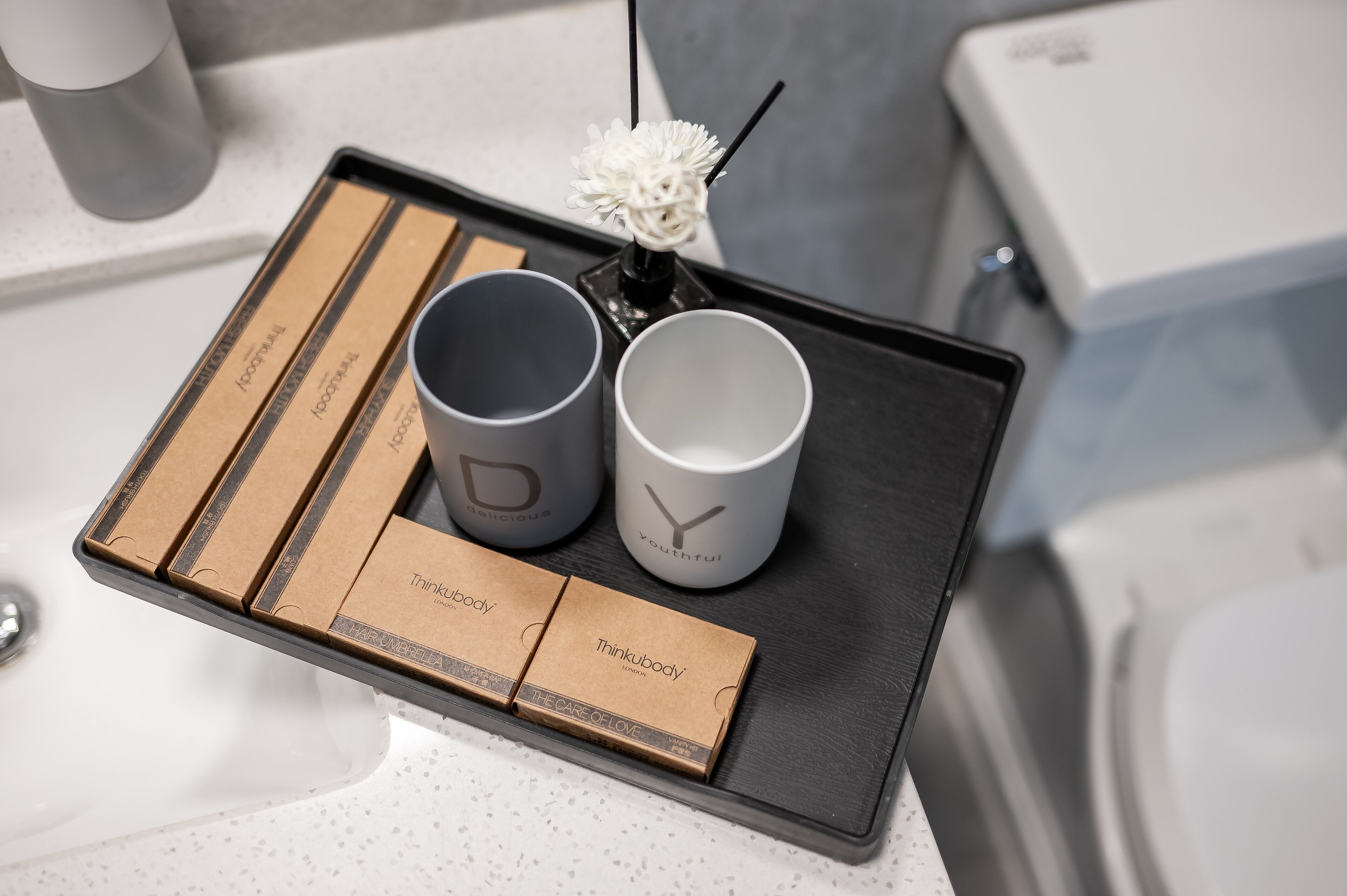 A tray with two gray mugs, a white vase with a floral arrangement, and a box labeled "Thinkbody" on a countertop.