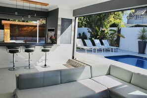 Un espacio exterior moderno con piscina, taburetes de bar y sillones de descanso.
