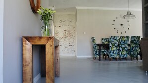 A modern living room with a wooden coffee table, a dining area with tropical chairs, and a brick accent wall.