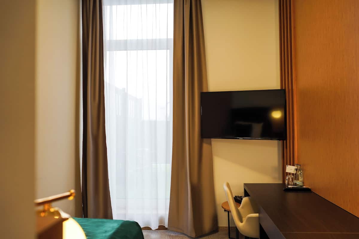 Hotelkamer met een bed, bureau, stoel, een aan de muur bevestigde televisie en een raam met gordijnen.
