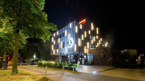 Un edificio moderno con cartel de cafetería, entrada pavimentada e iluminación exterior intensa por la noche.
