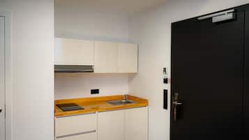 Una cocina compacta con armarios blancos, una encimera de madera, un fregadero de acero inoxidable y una puerta negra.
