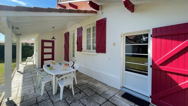 A covered patio with a table and chairs, a white door with red shutters, and a red garage door.