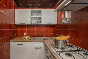 A kitchen with red tiles, white cabinets, a gas stove, and a sink.