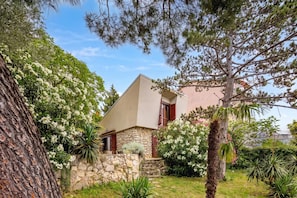 A house with a stone wall, a wooden door, and a small garden with various plants and trees. - Lovely Holiday Home By The Sea (Crikvenica)