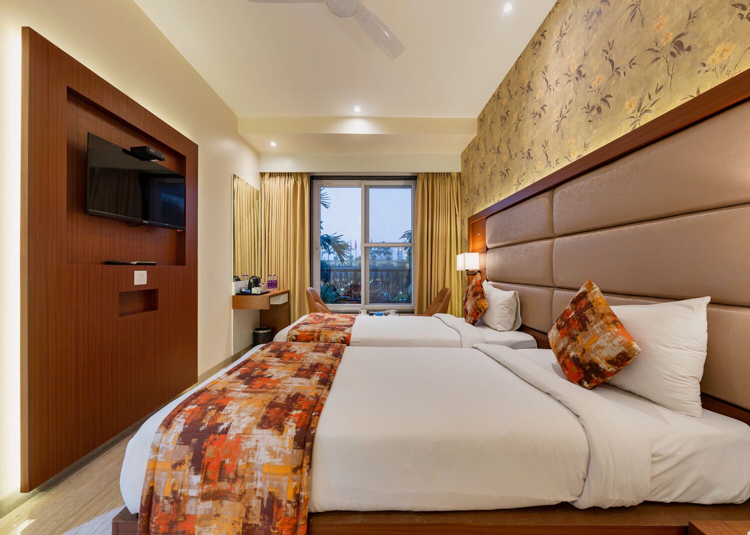 Habitación de hotel con dos camas, televisión montada en la pared, escritorio con silla y ventana con cortinas.