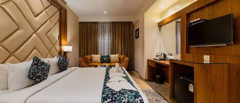 Una habitación de hotel con una cama grande, un escritorio con televisión de pantalla plana, un ventilador de techo y un minibar.