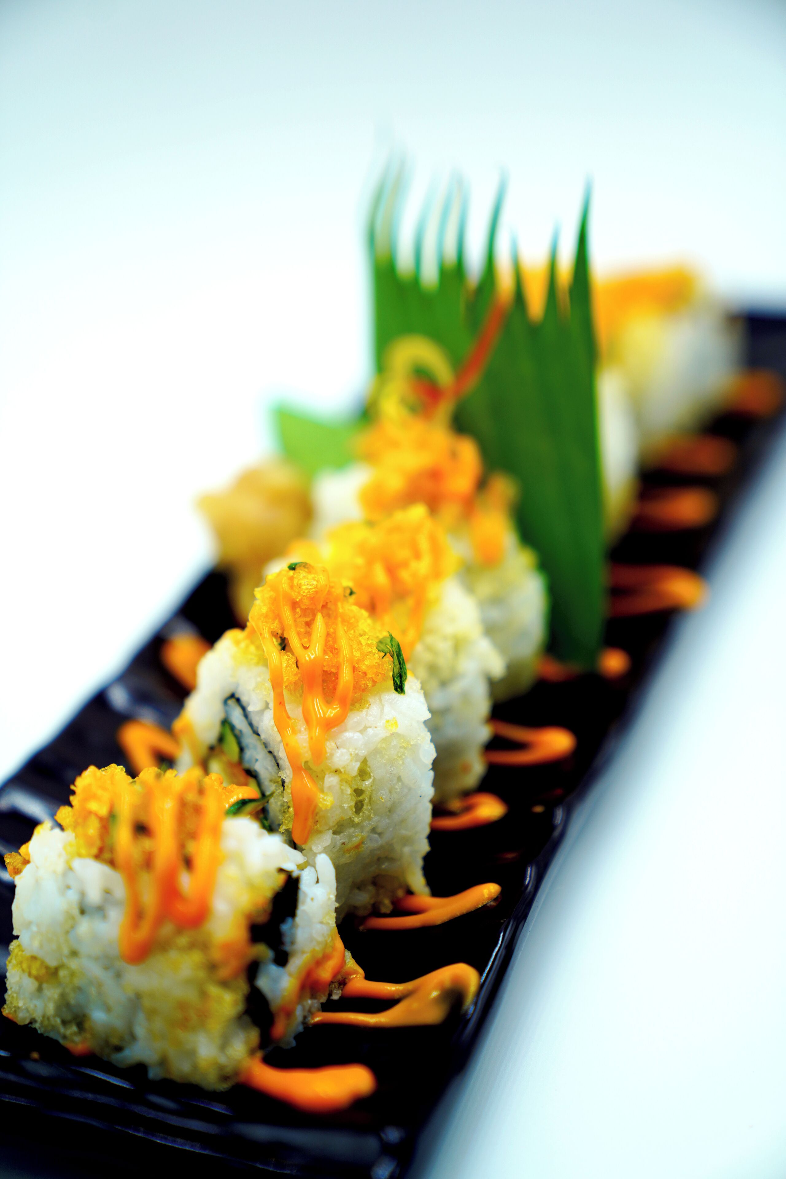 A sushi dish with orange sauce and green garnish on a black plate.