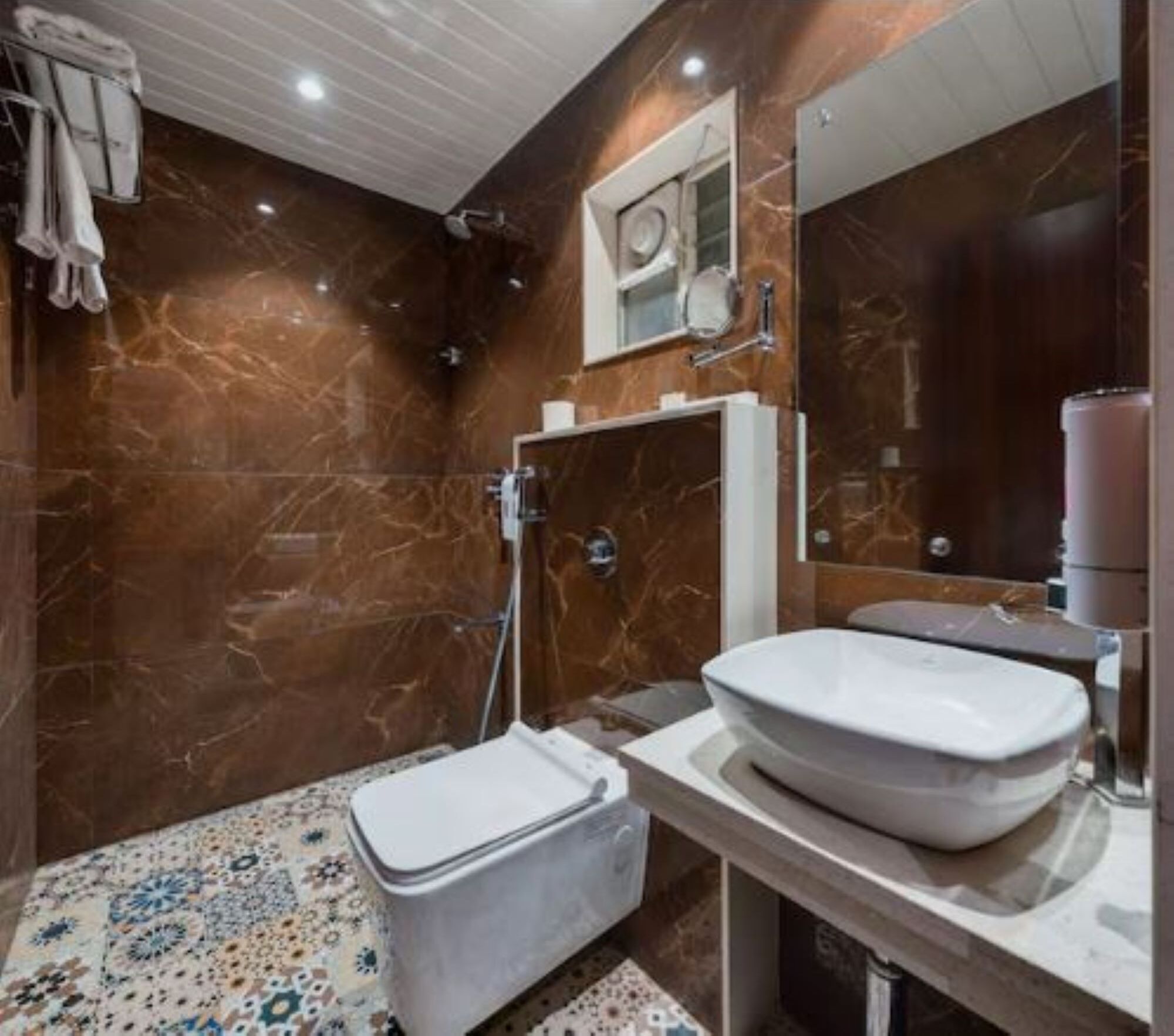 Un baño con pared de mármol, un lavamanos blanco y un inodoro.