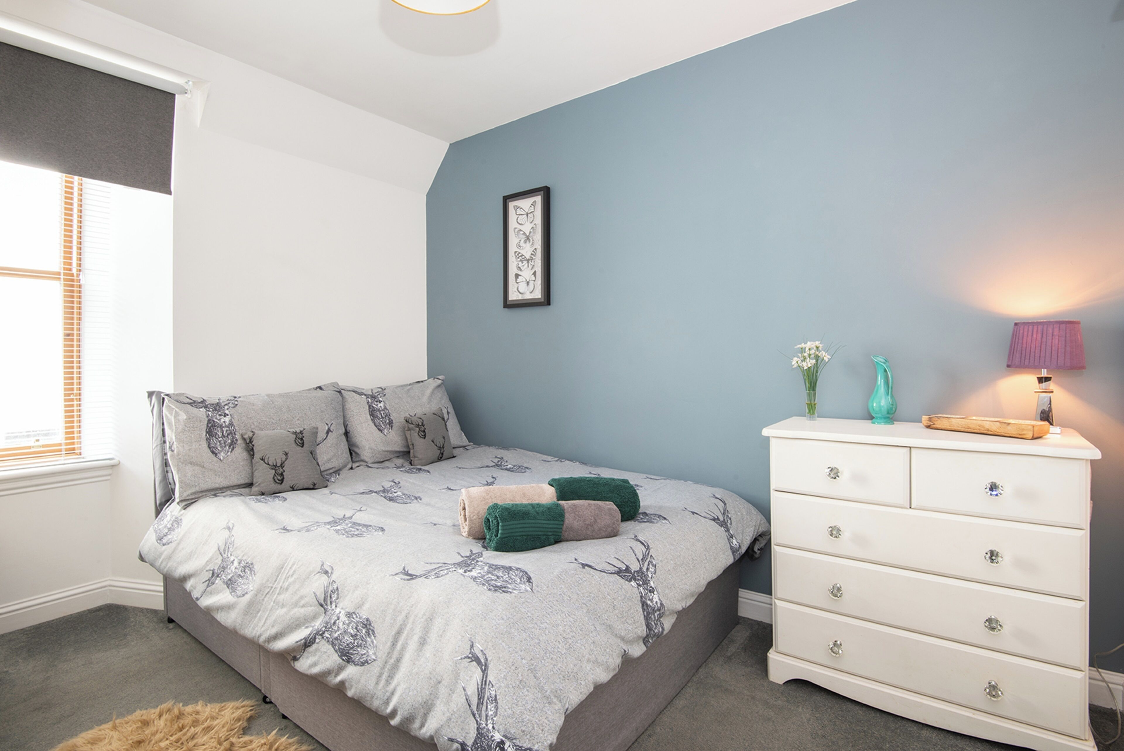 Un dormitorio con cama, cómoda, cuadro enmarcado y ventana con persianas.