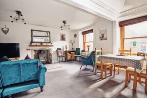 Una sala de estar acogedora con un sofá azul, una mesa de comedor de madera y sillas. Hay una chimenea, un televisor y un espejo grande en la pared.
