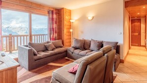 A cozy living room with a sofa set, a small table, and a view of mountains through large windows. - Ski-in/ski-out apartment, 4 bedrooms, 8 ppl, covered parking, WiFi (Les Arcs 1800)