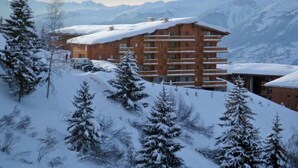 A multi-story hotel with a sloped roof, surrounded by snow-covered trees and mountains. - Ski-in/ski-out apartment, 4 bedrooms, 8 ppl, covered parking, WiFi (Les Arcs 1800)