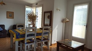A dining area with a table and chairs, a lamp, and a window with curtains. - Logement Calme et Spacieux Avec vue à 400 M D'un Plan D'eau (Lamastre)