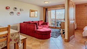 Un cuarto acogedor con un sofá rojo, una mesa de comedor de madera y vistas a las montañas a través de un gran ventanal corredera.