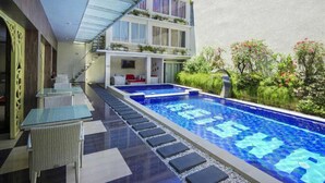 Uma área de piscina moderna ao ar livre com teto de vidro, escadaria que leva a um segundo andar e um jardim exuberante com diversas plantas e flores.