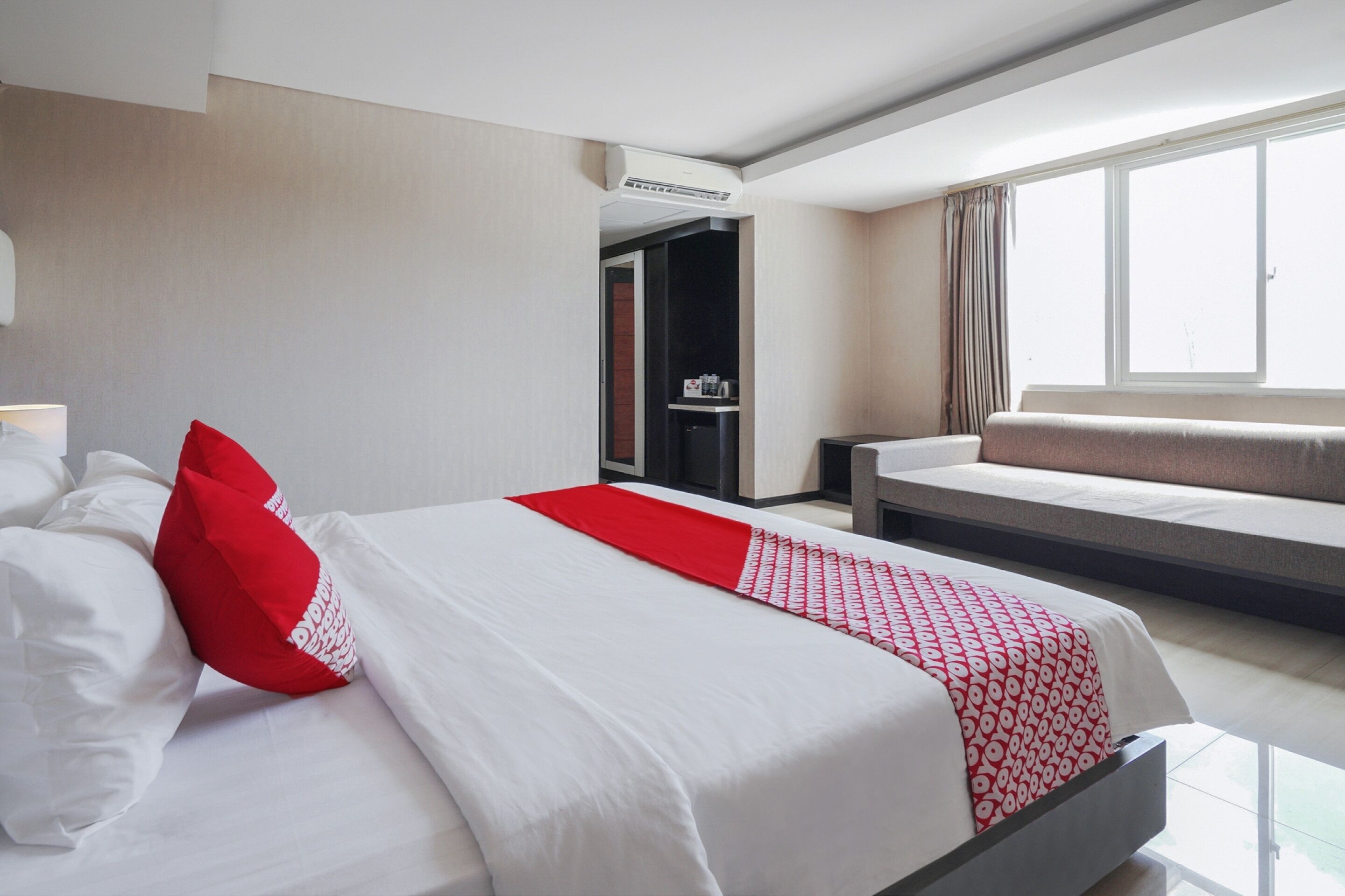 A hotel room with a bed, a sofa, a window, and an air conditioning unit.