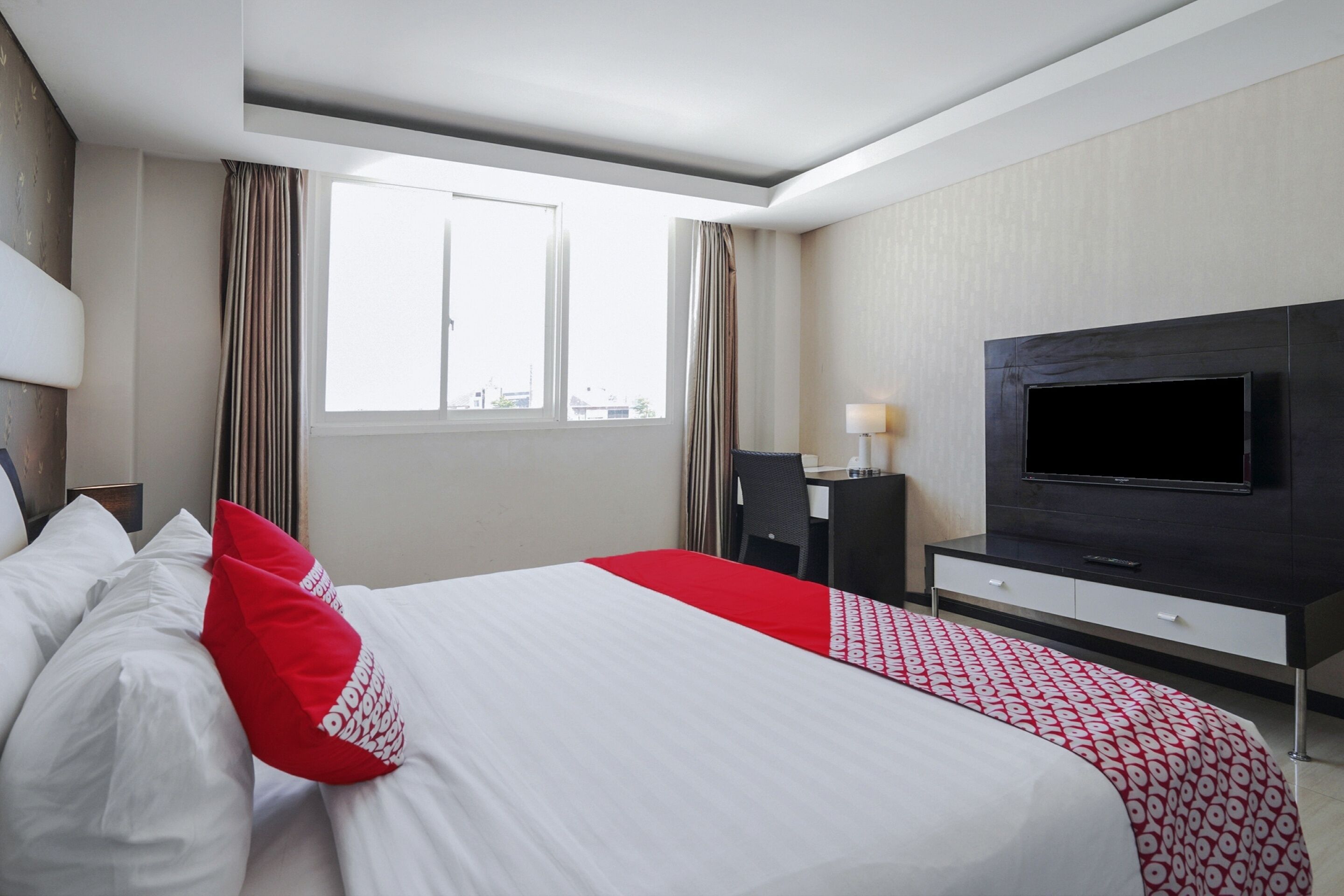 A hotel room with a large bed, a TV, a desk, and a window.