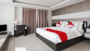 Quarto de hotel moderno com uma cama grande, uma escrivaninha com cadeira, televisão e cortinas.