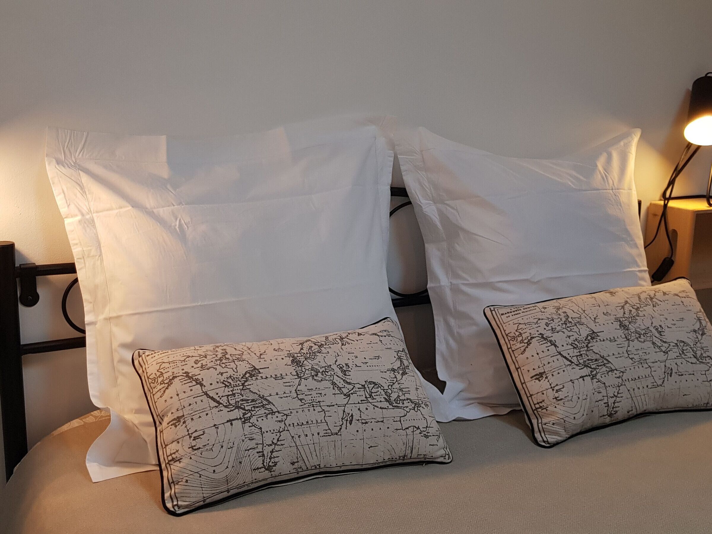 A bed with white pillows and two decorative pillows featuring a world map design.
