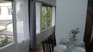 Un coin repas avec une table dressée pour quatre personnes, de grandes fenêtres avec des rideaux et une vue sur un jardin.
