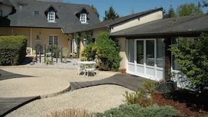 Une maison dotée d’un patio couvert, d’un espace recouvert de gravier et d’un petit jardin agrémenté d’une terrasse en bois.