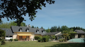 Une grande maison avec de nombreuses pièces, un patio couvert et une pelouse bien entretenue.