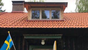 A wooden building with a tiled roof, a flag, and potted plants. - Cottage with fantastic lake view!  (vittsjö)