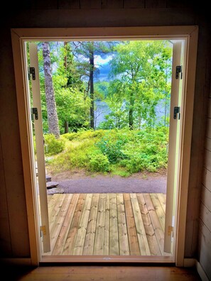 A wooden deck leading to a door with a view of a forest and a lake. - Cottage with fantastic lake view! (vittsjö)