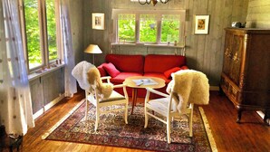 A cozy room with a red sofa, two white chairs, a small round table, and a wooden cabinet. - Cottage with fantastic lake view!  (vittsjö)