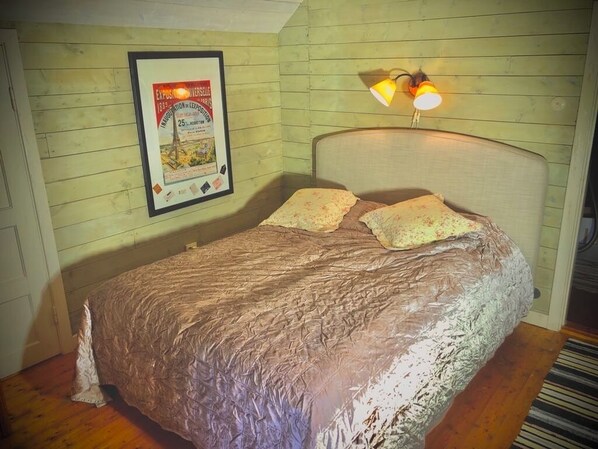 A bedroom with a bed, a headboard, a wall-mounted lamp, and a framed poster. - Cottage with fantastic lake view! (vittsjö)