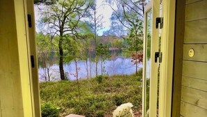 A wooden door leading to a deck with a table and chairs, overlooking a lake and trees. - Cottage with fantastic lake view!  (vittsjö)
