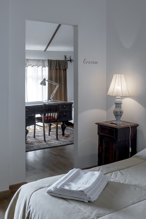 A bedroom with a bed, a desk with a chair, a lamp, and a small cabinet.