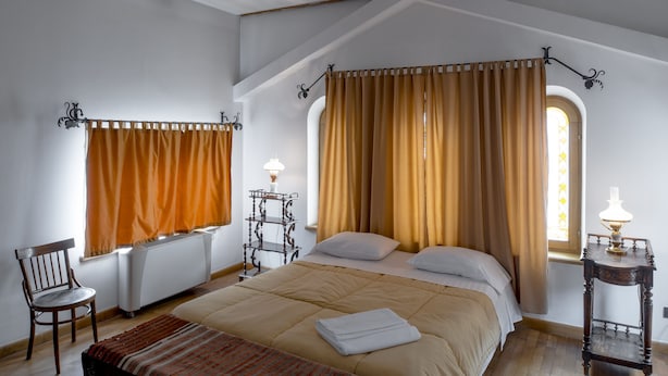 A bedroom with a large bed, two bedside tables, a chair, and a window with curtains. - Villa Ayghedzor (Yerevan)