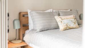 Una cama bien hecha con ropa de cama a rayas y un cojín decorativo, una lámpara de noche y una mesita de noche de madera.