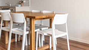 Una mesa de comedor con cuatro sillas blancas, suelo de madera y una cocina al fondo.